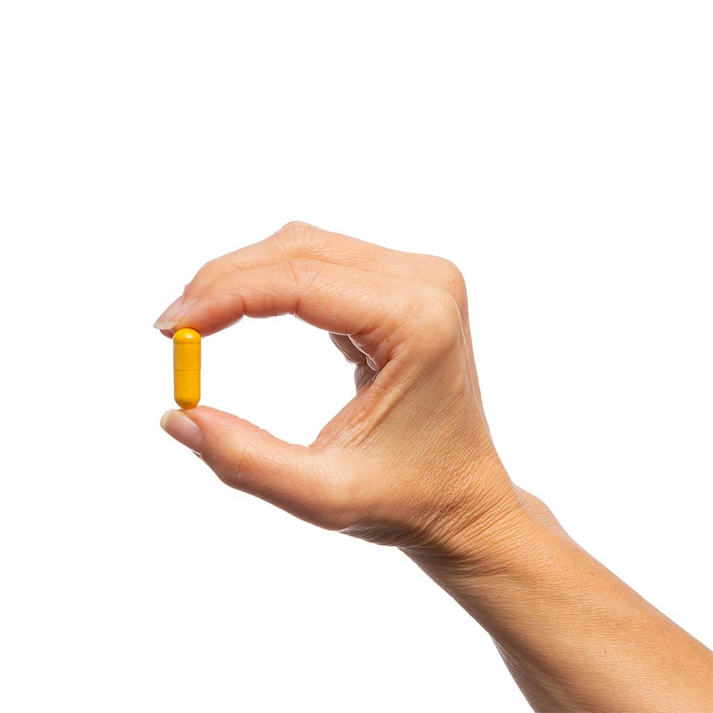 Hand holding a yellow supplement capsule against a white background