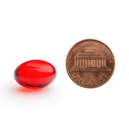 Red capsule next to a U.S. penny on a white background