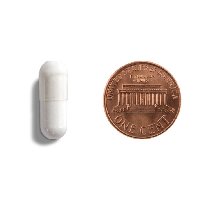 White capsule pill next to a copper penny on a white background