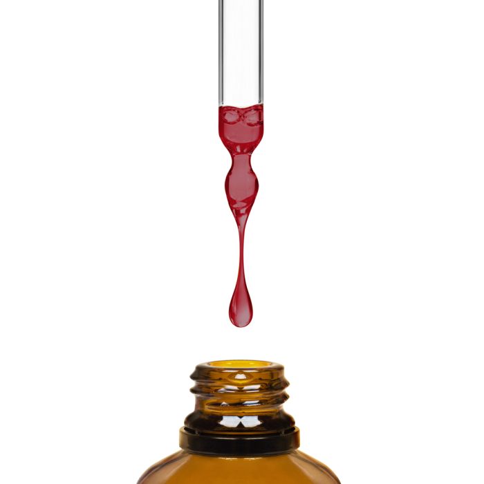 Red liquid being dripped from a dropper into an amber bottle on a white background
