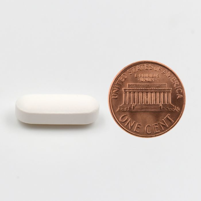 White pill next to a U.S. penny on a white background