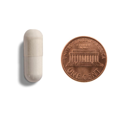 White capsule pill next to a U.S. penny on a white background
