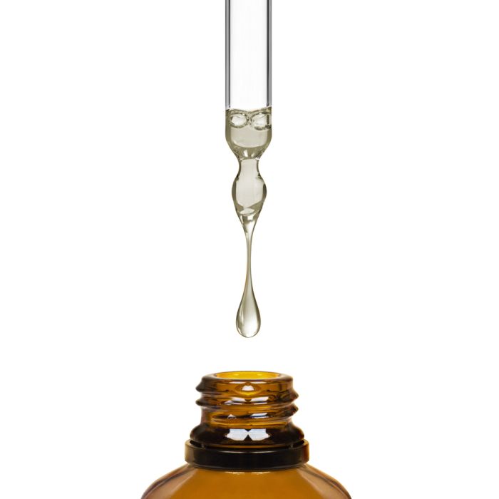 Glass dropper with a drop of liquid over an amber bottle on a white background