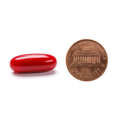 Red capsule next to a U.S. penny on a white background