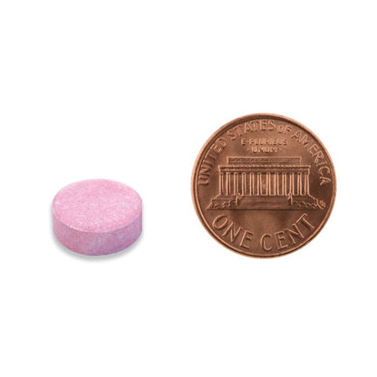 Pink pill next to a U.S. penny on a white background