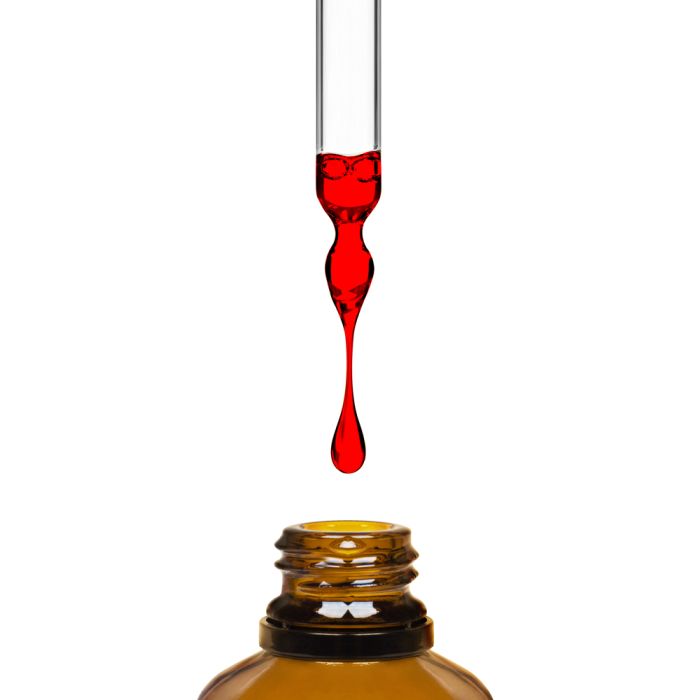 Red liquid being dripped from a dropper into an amber bottle on a white background