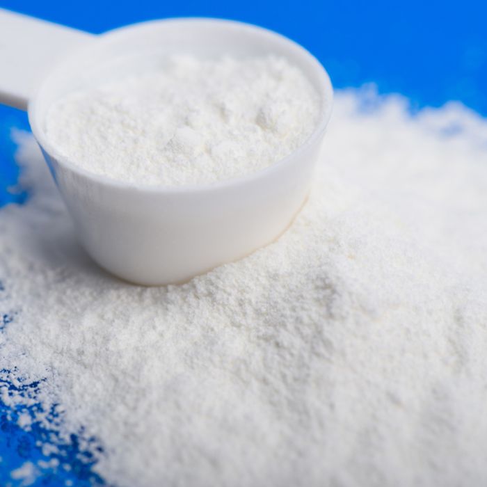 White powder in a white bowl with a white scoop on a blue background