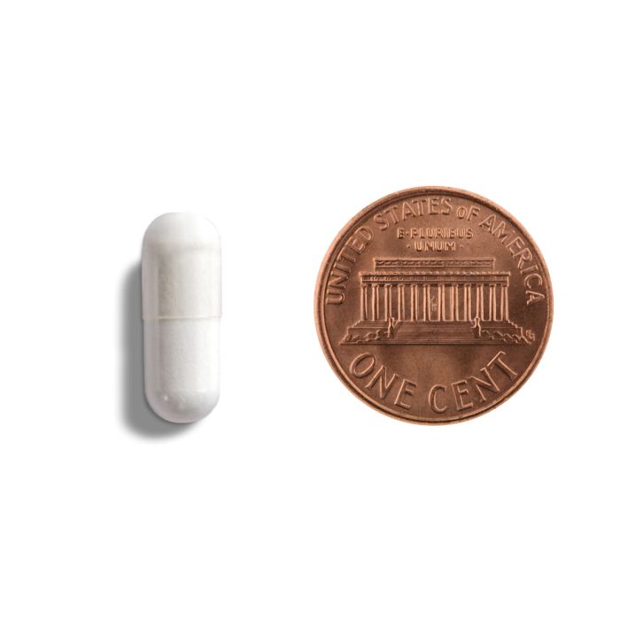 White pill next to a U.S. penny on a white background