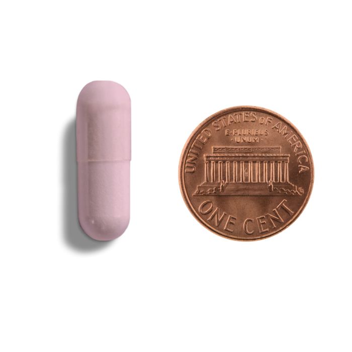 Pink capsule-shaped object next to a U.S. penny on a white background
