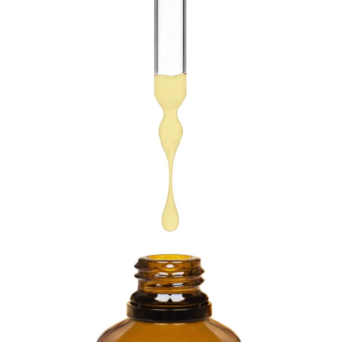 dropper with yellow liquid dripping into a brown bottle on a white background