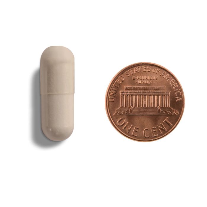 White capsule pill next to a U.S. penny on a white background
