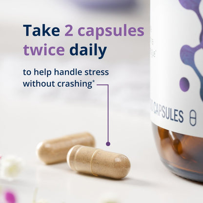 Two beige supplement capsules on a white surface next to a white bottle with purple graphics, with text reading 'Take 2 capsules twice daily to help handle stress without crashing'.
