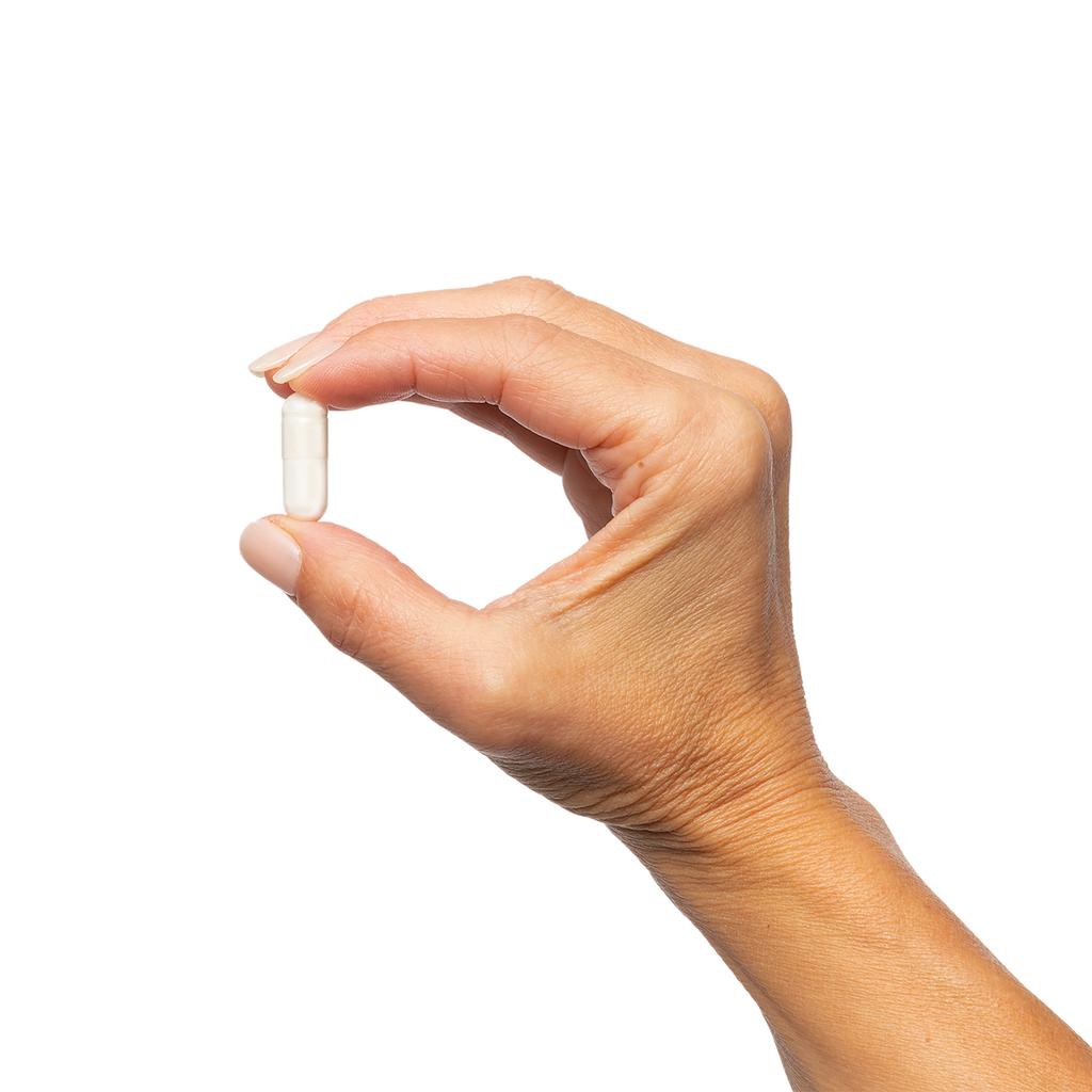Hand holding a white pill against a white background
