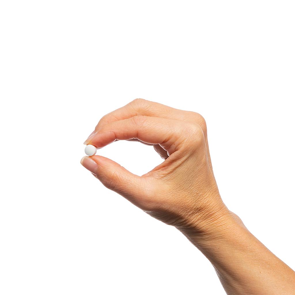 Hand holding a white pill against a white background