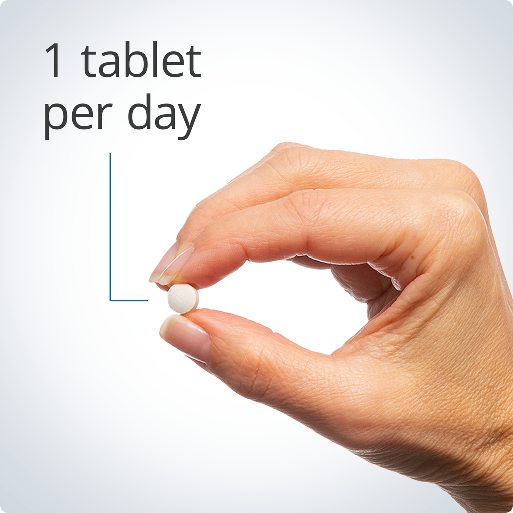 Hand holding a white pill with text '1 tablet per day' on a light gray background