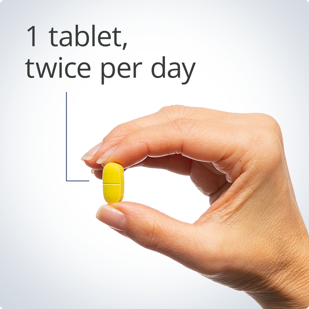 Hand holding a yellow tablet with text '1 tablet, twice per day' on a light gray background