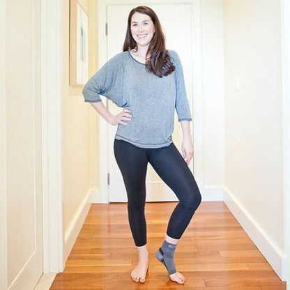 Woman wearing a gray sweater and black leggings standing in a hallway.
